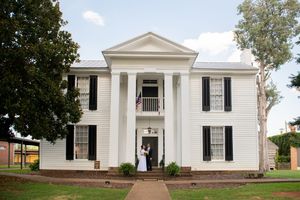 Exterior view of a grand white colonial style building with columns and black shutters.