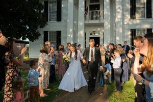 Wedding party and guests gathered outside a historic white mansion during evening celebration.