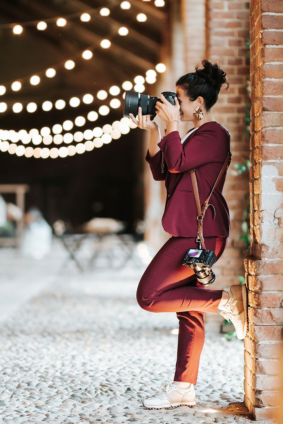 Female photographer in burgundy outfit crouches to take photos with DSLR camera at an outdoor venue.