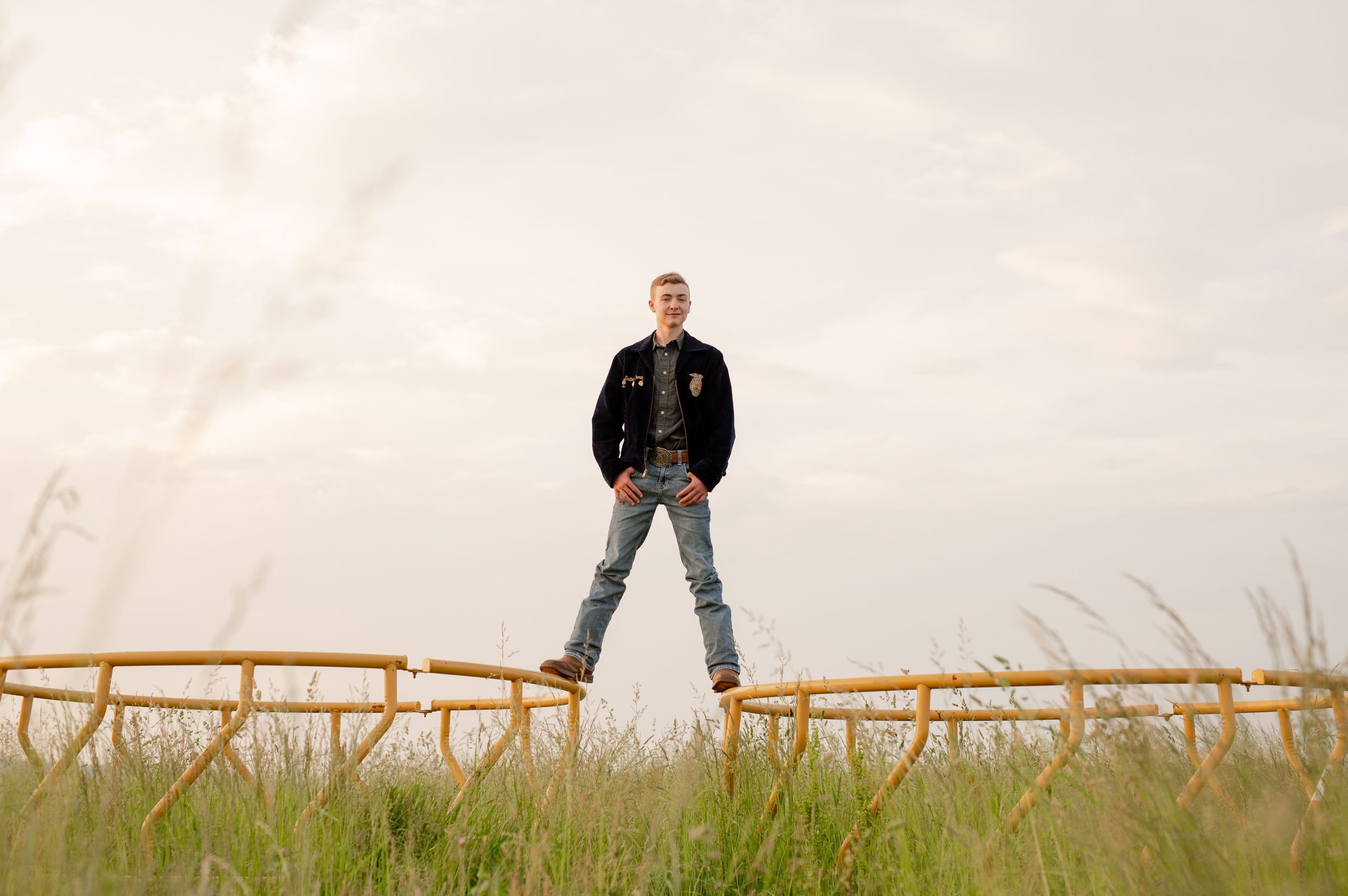 Person stands confidently on wooden fence in rural field during sunset.