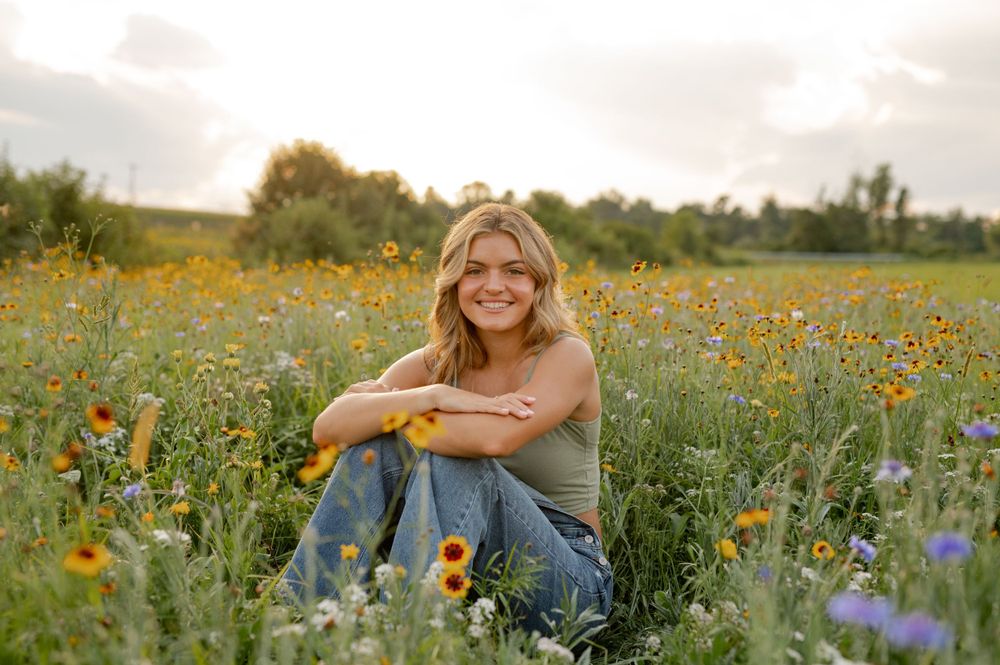 Person sitting in wildflower meadow filled with yellow and purple blooms during golden hour.