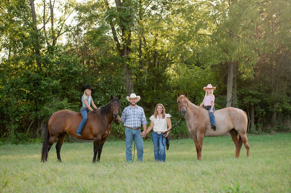 Family group poses with horses in green pasture during golden hour.