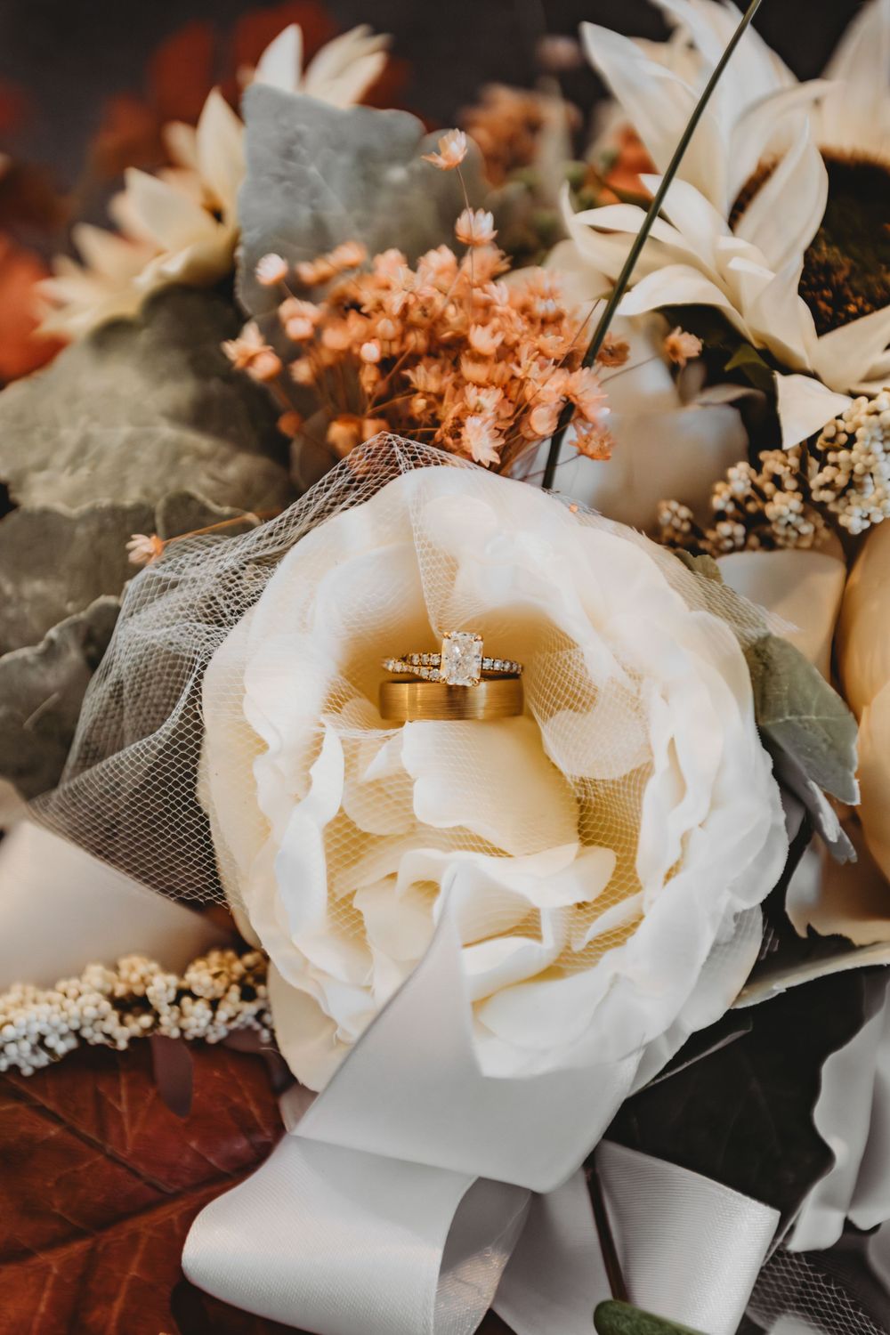 Close-up of wedding rings nestled in a white rose with autumn-colored florals.