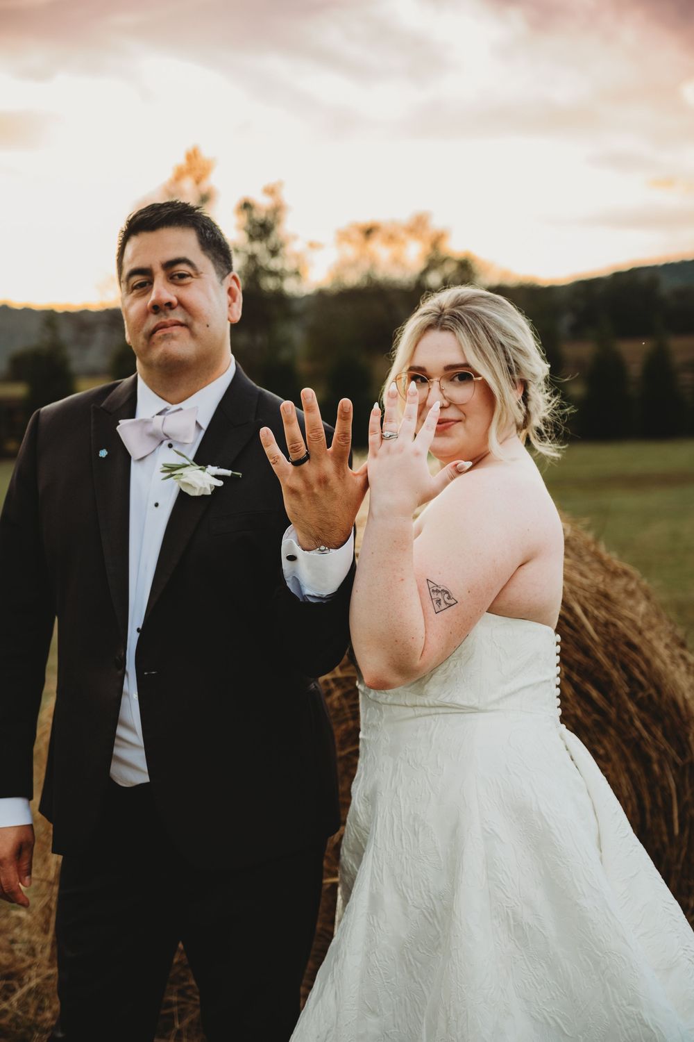 Playful newlyweds share a joyful candid moment laughing together in a rustic outdoor setting at sunset.