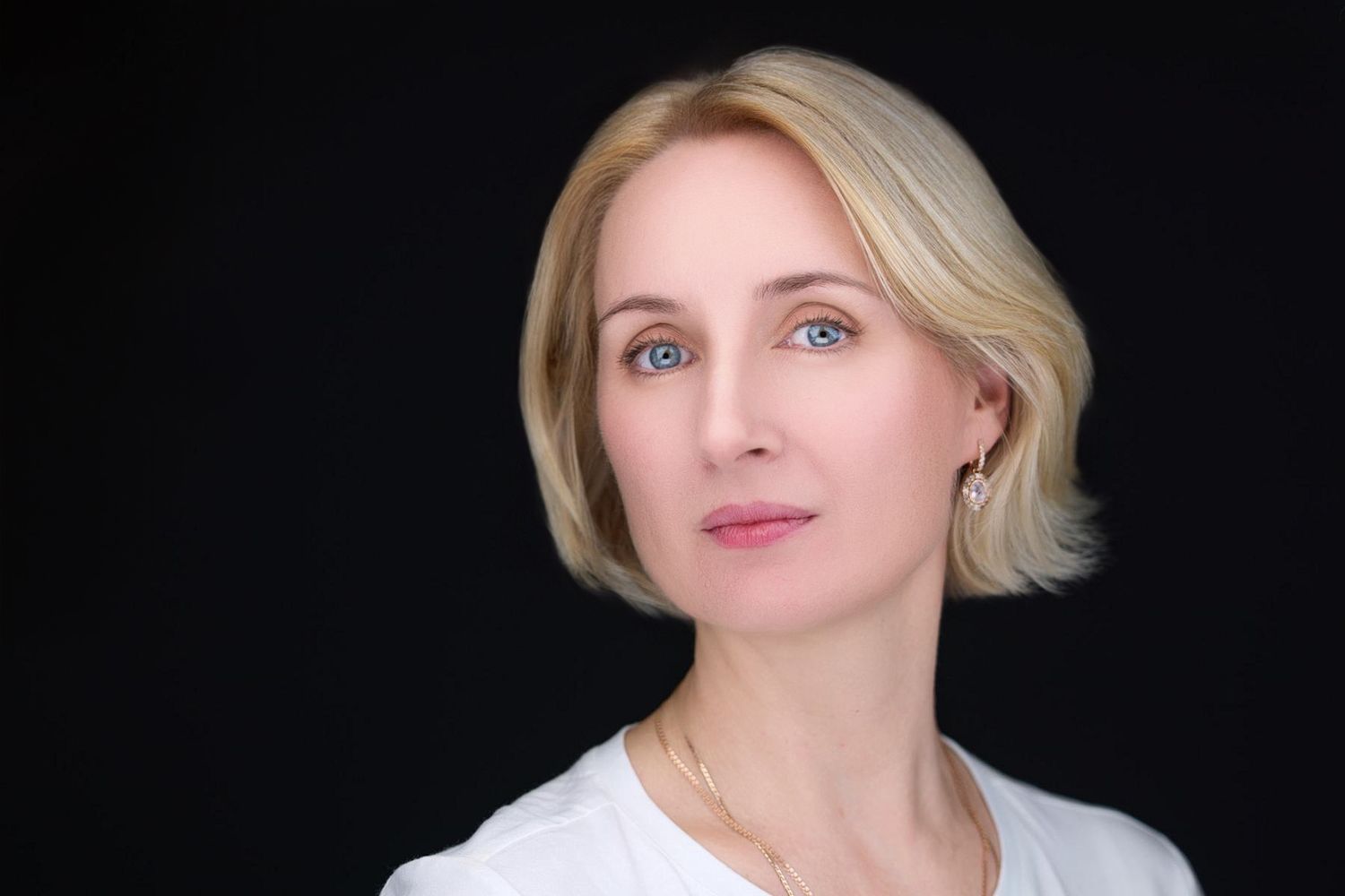 Professional headshot against black background with simple white top.