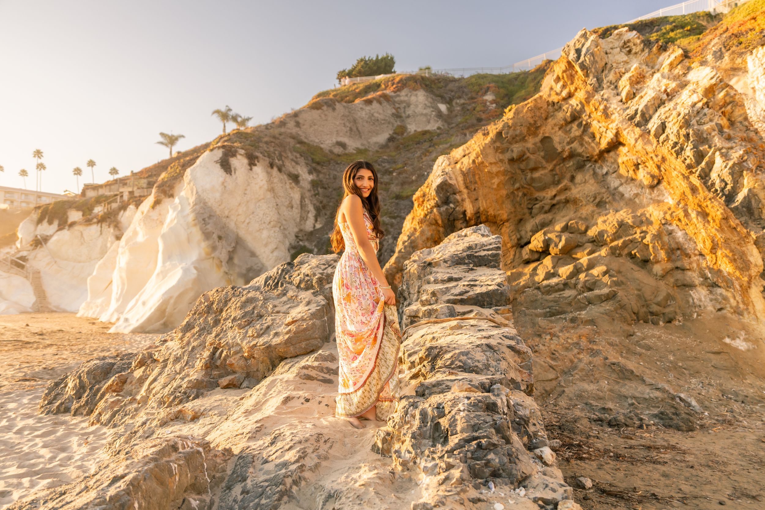 Person in orange dress climbs ancient stone steps against sandstone cliff face.