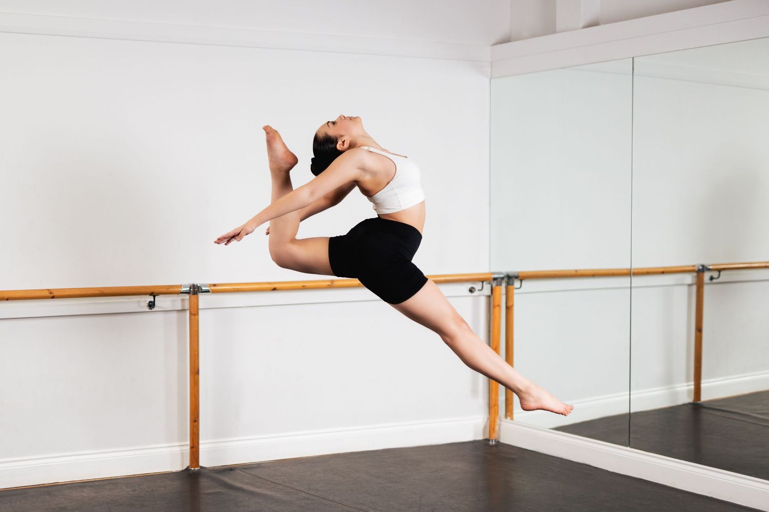 Dancer in split pose against glass wall wearing black leggings and white crop top.
