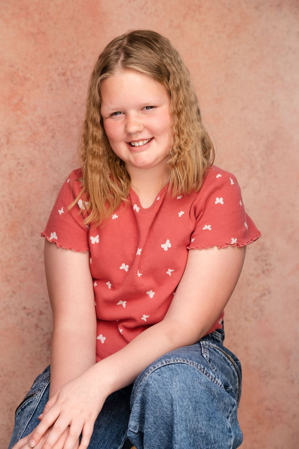 Portrait series against pink background showing casual pose in coral patterned top and jeans.