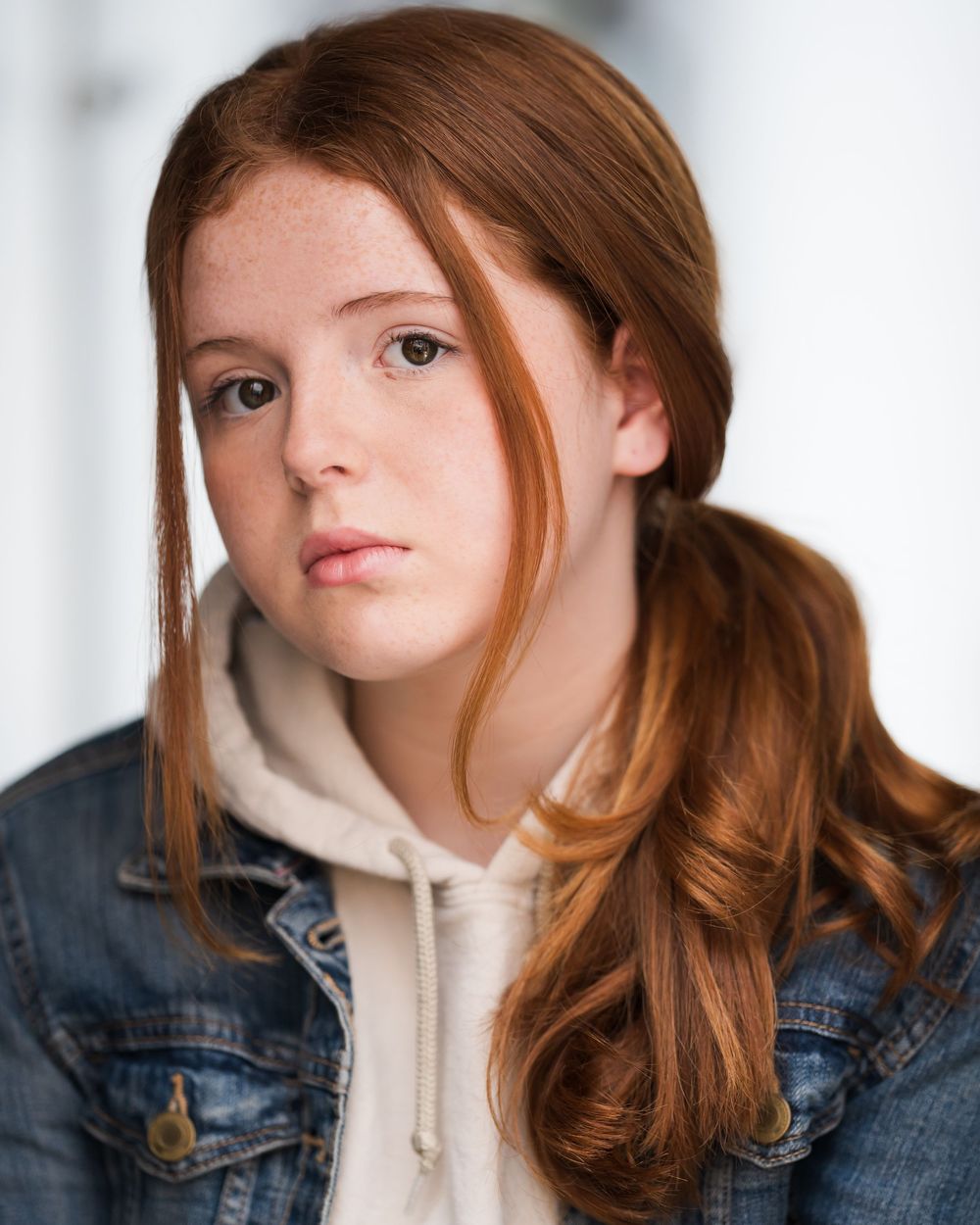 A person wearing a denim jacket and white hoodie poses against a light background in a series of close-up shots.