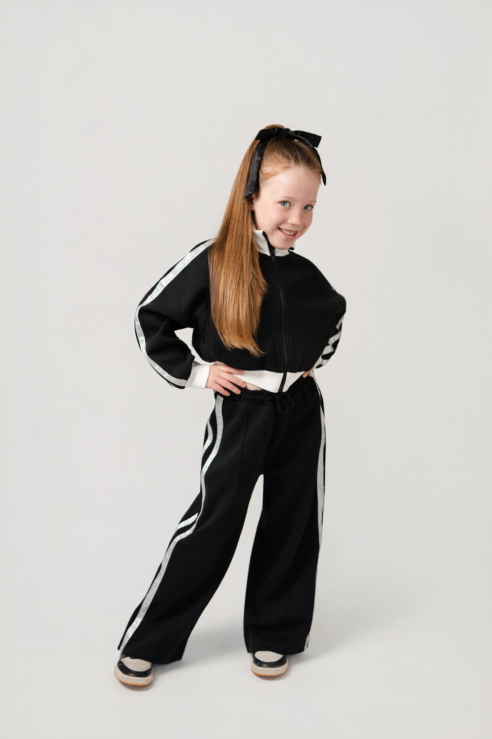 A child in a black and white tracksuit poses playfully against a white studio backdrop.
