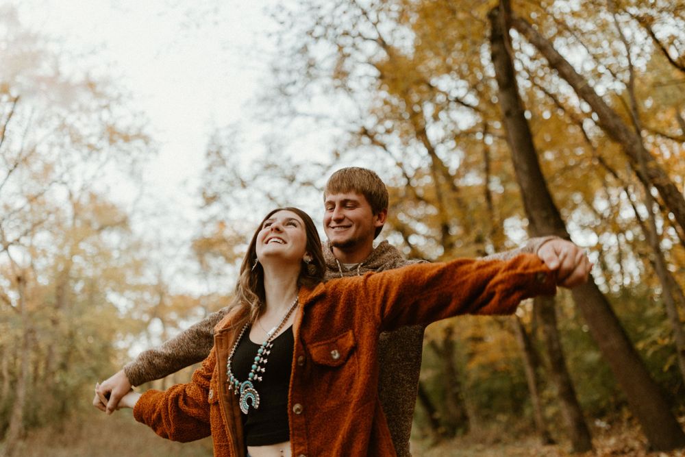 Two people with arms outstretched enjoying autumn day under golden trees.