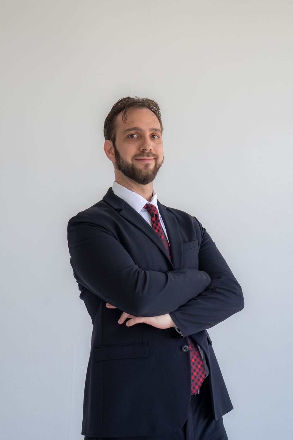 Business professional in suit and red tie poses confidently against white wall.