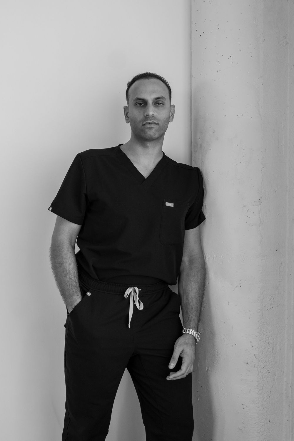 Healthcare professional in black scrubs poses against white wall for portrait series.