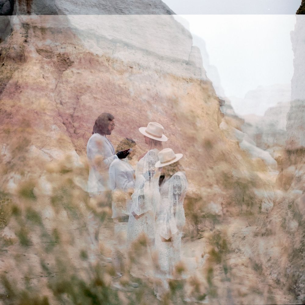 A dreamy double exposure photo of a family in white clothing among desert rock formations and wildflowers.