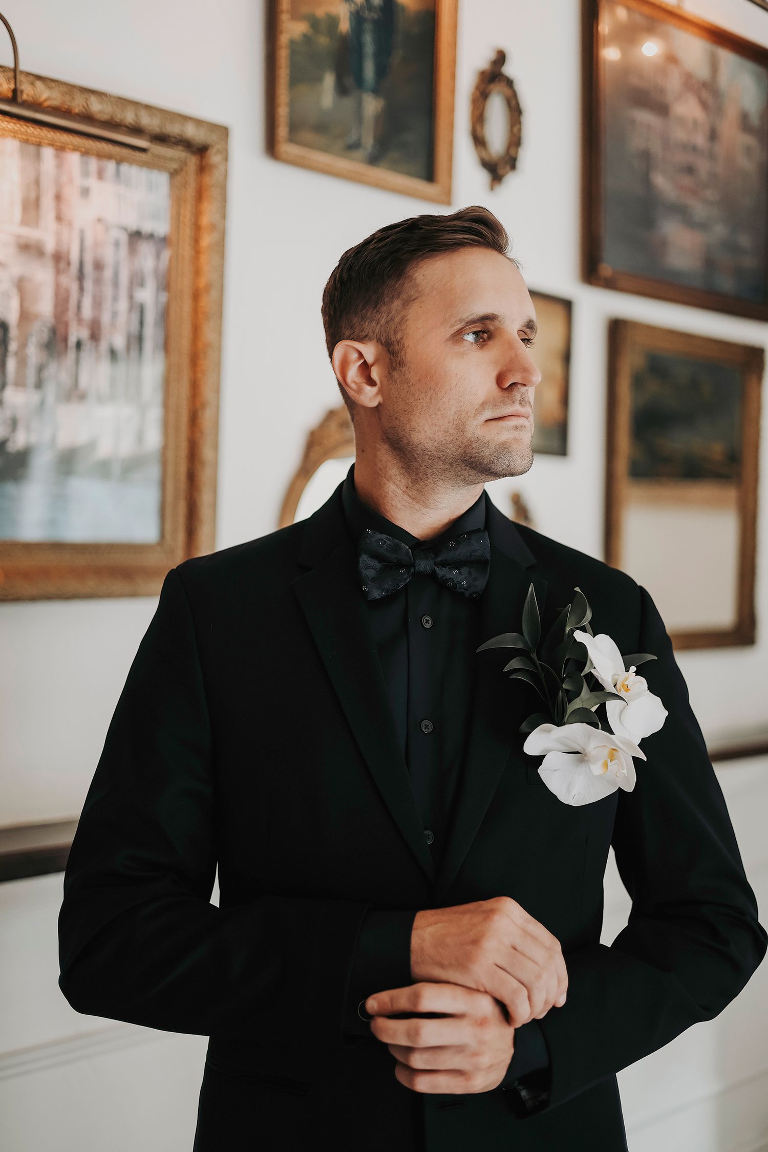 the dapper groom gets ready as he puts on his black suit and bowie in the natural lighting