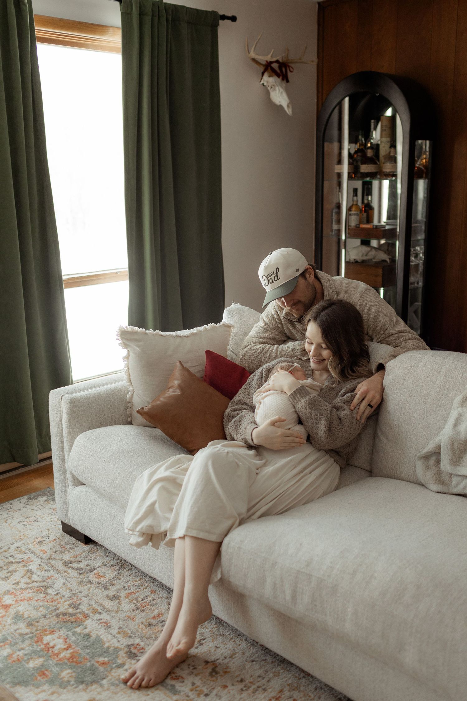 A couple shares a tender moment on a brown couch against mint green floral wallpaper.