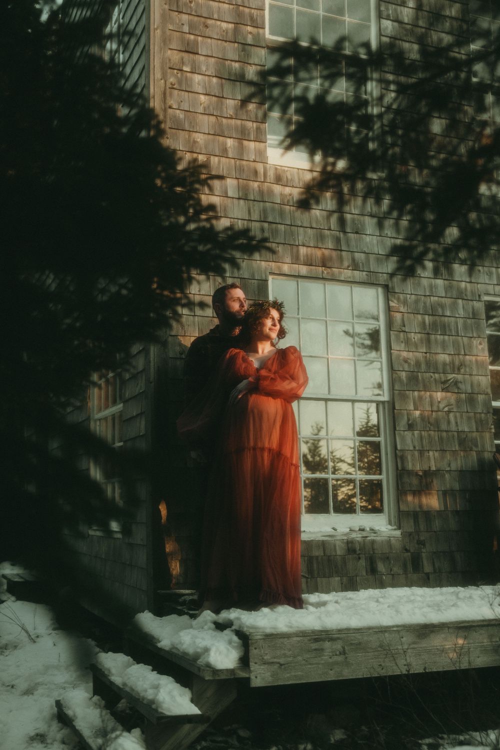 A couple in winter attire embraces against a brick wall with snow on the ground.