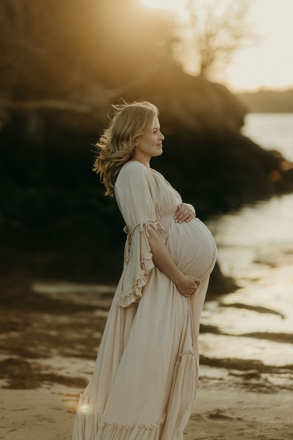 Silhouetted maternity portrait at sunset with flowing dress against waterfront backdrop.