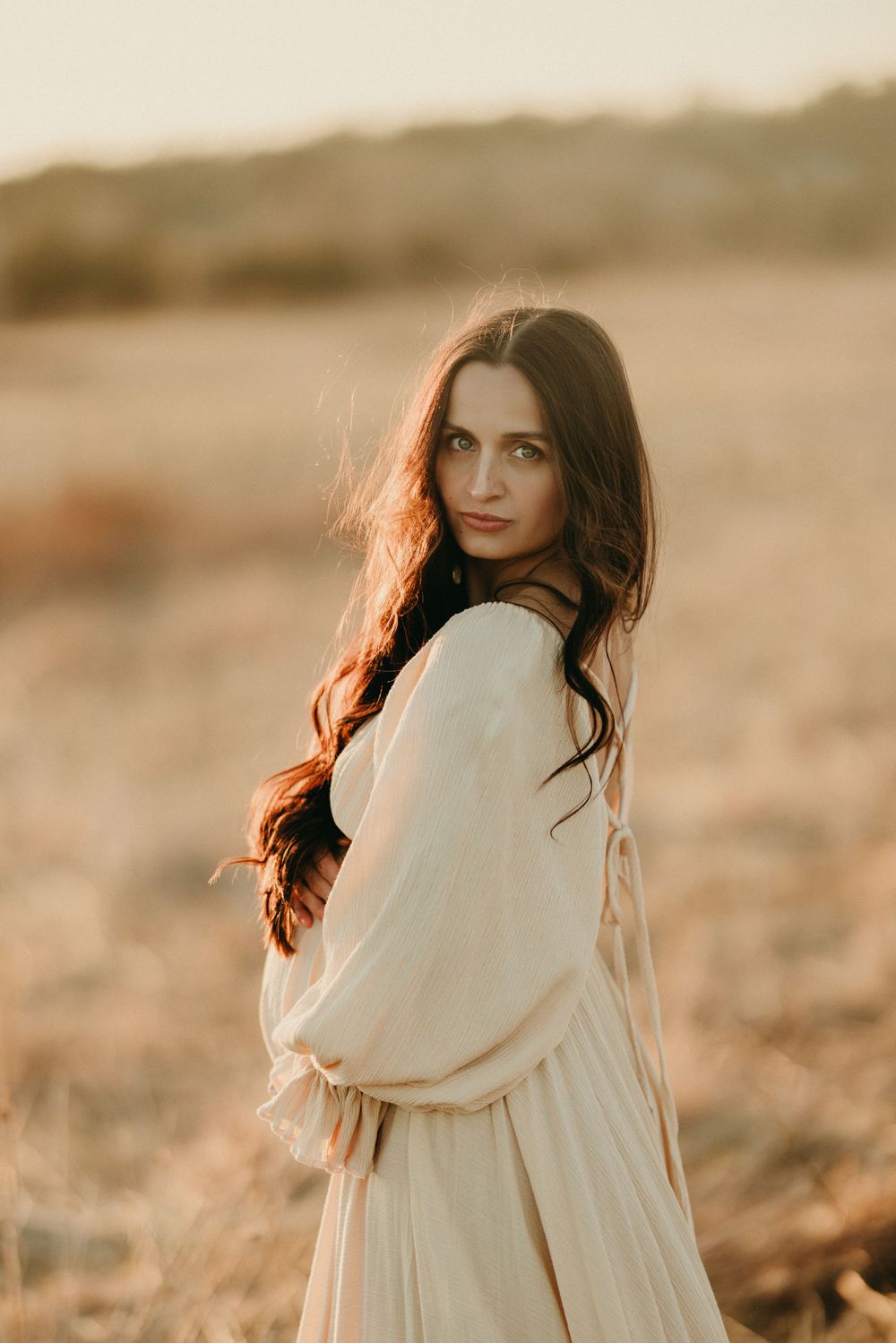 Ethereal portrait of woman in cream sweater with windswept hair in warm natural lighting.