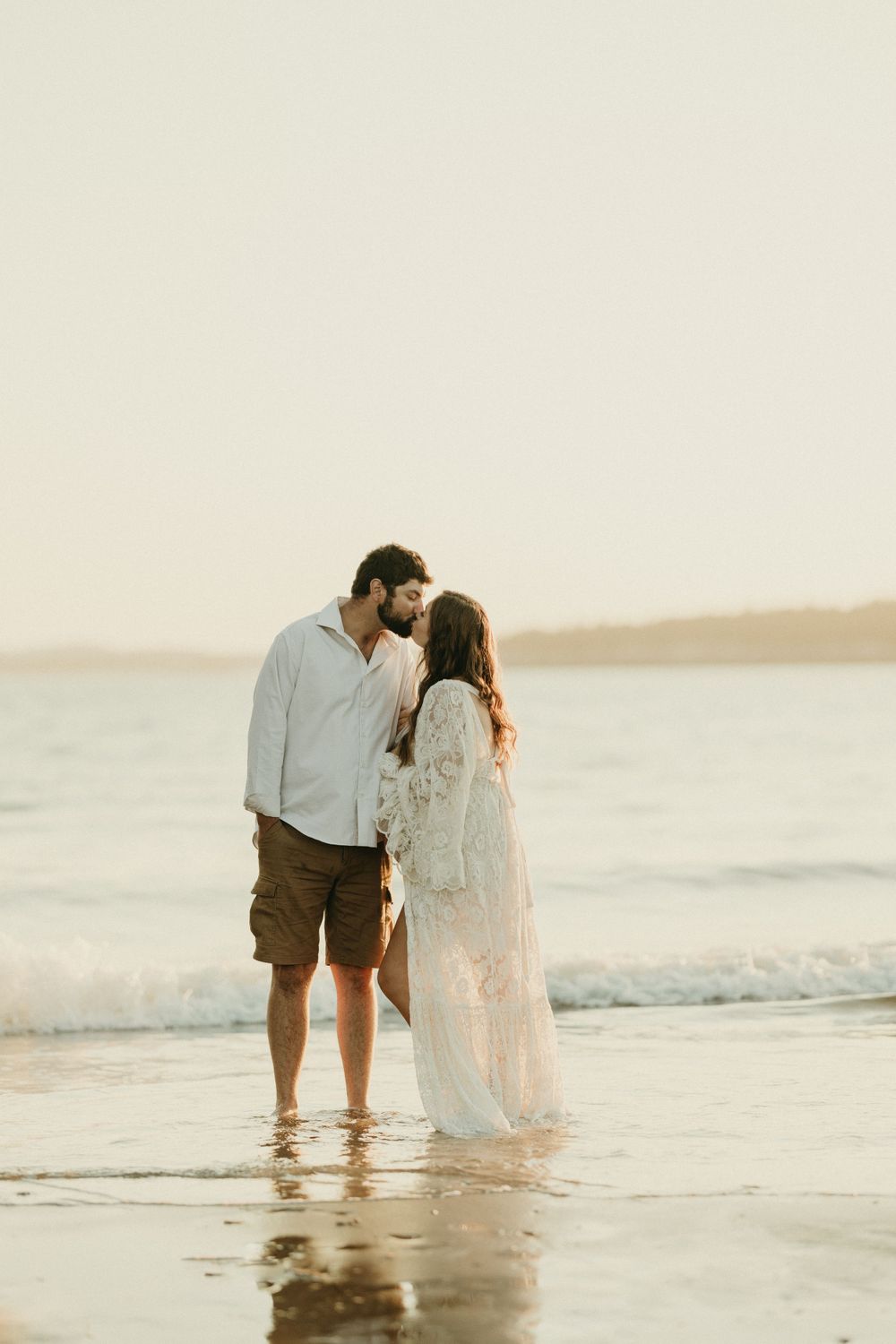 Couple standing in shallow ocean waters during sunset wearing beach formal attire.