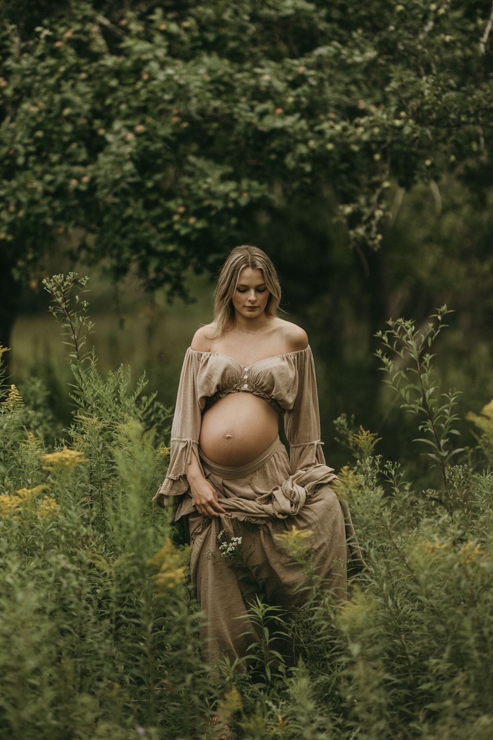 Ethereal maternity portraits among wildflowers with woman wearing a draped beige gown.