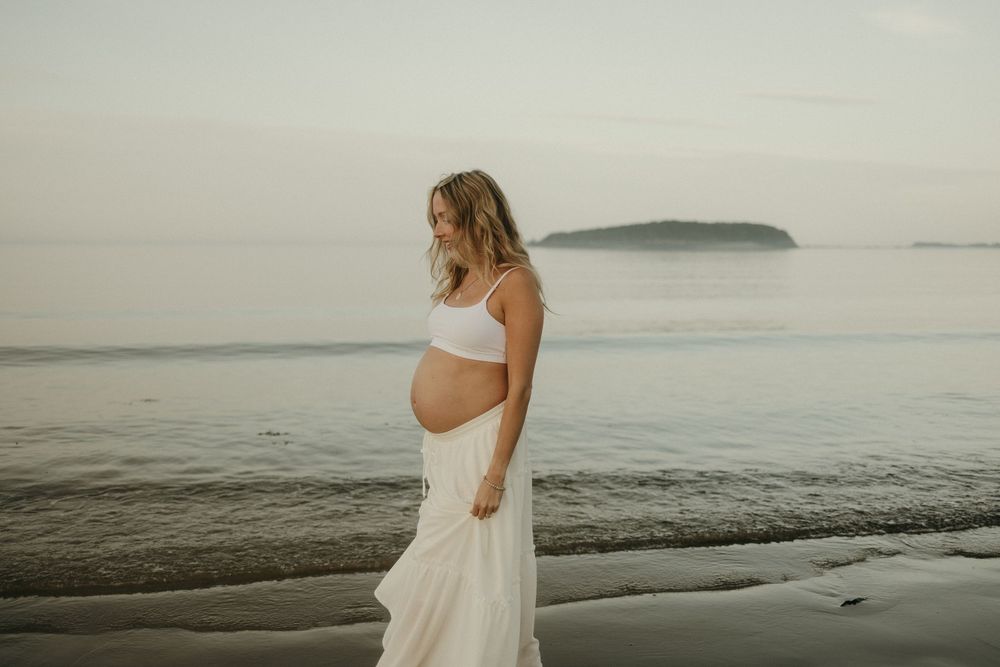 A peaceful maternity portrait showcases a white dress against the ocean waves.