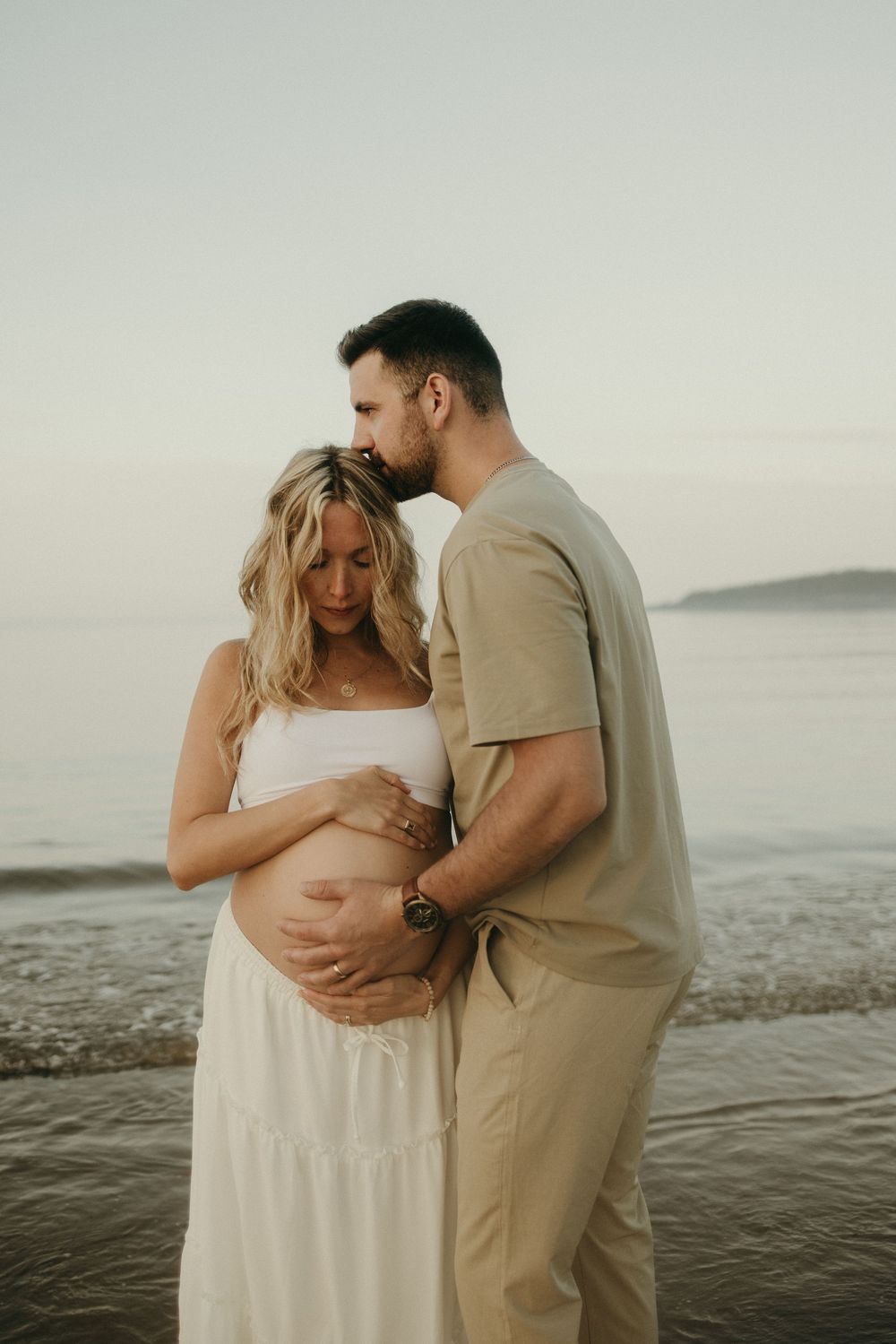 An intimate maternity photo captures a couple's tender moment by the ocean.