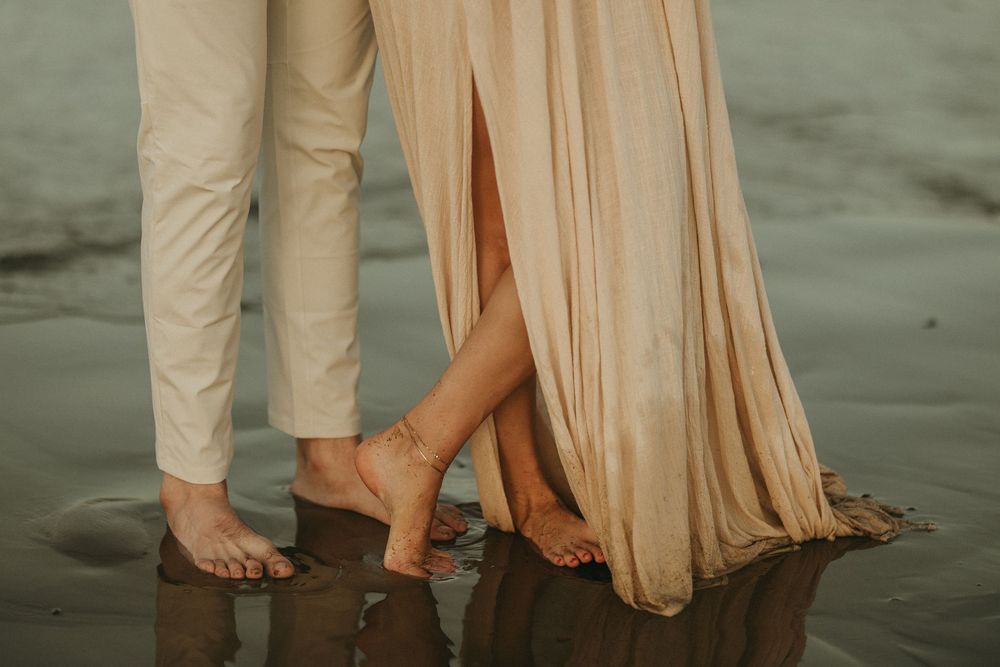 Bare feet and flowing dress hem standing in wet sand at the beach.