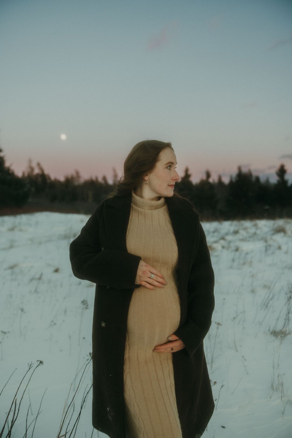 Winter landscape photography with figure in beige dress against snowy field at dusk.