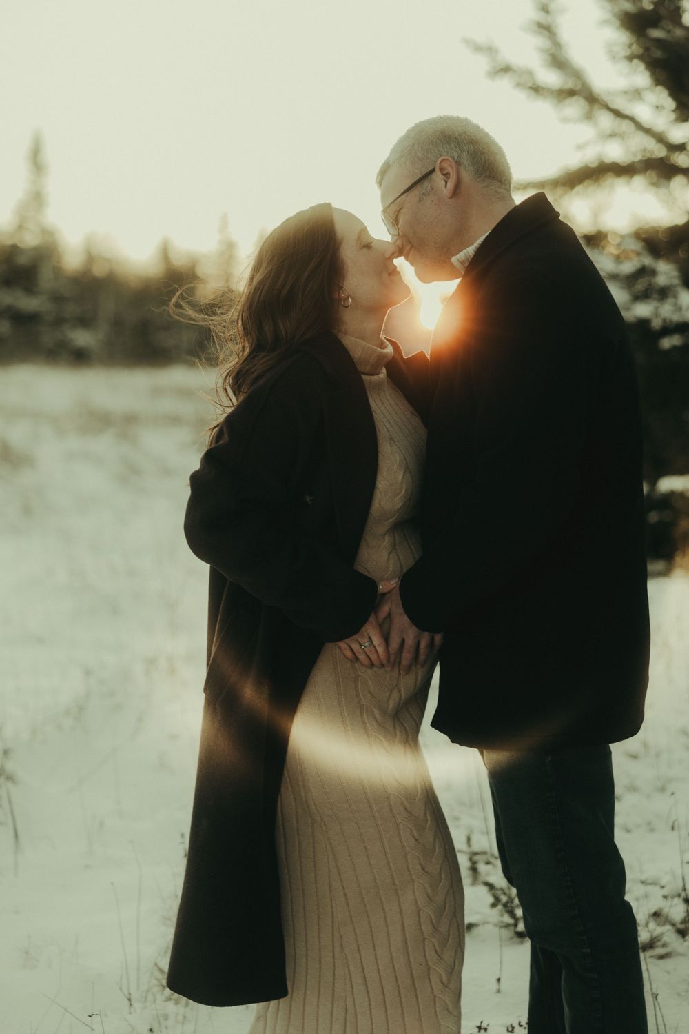 Intimate winter couples photoshoot with golden sunset light in snowy landscape.