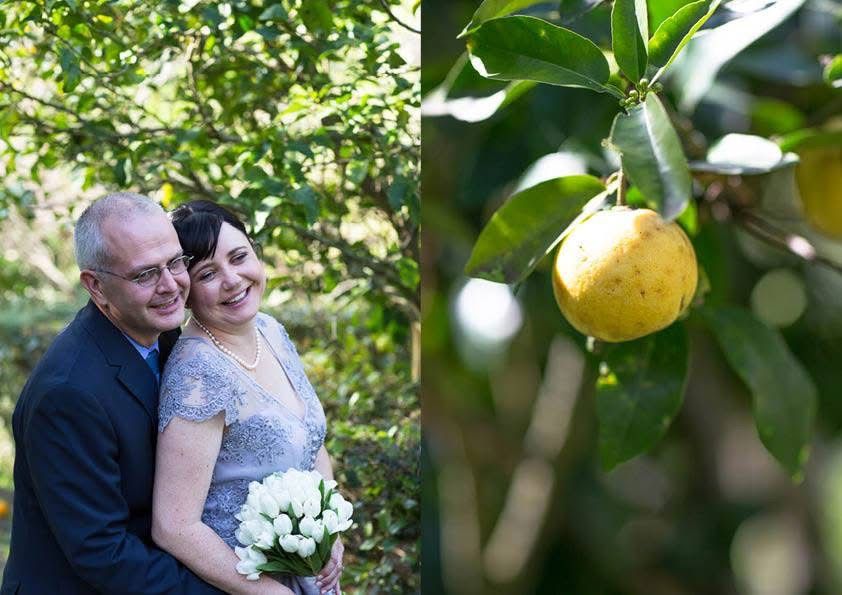 Happy couple embraces outdoors on wedding day beside a yellow lemon hanging from a tree.