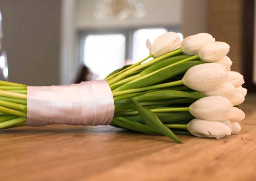 Elegant bridal bouquet of white tulips tied with ribbon resting on wooden table.