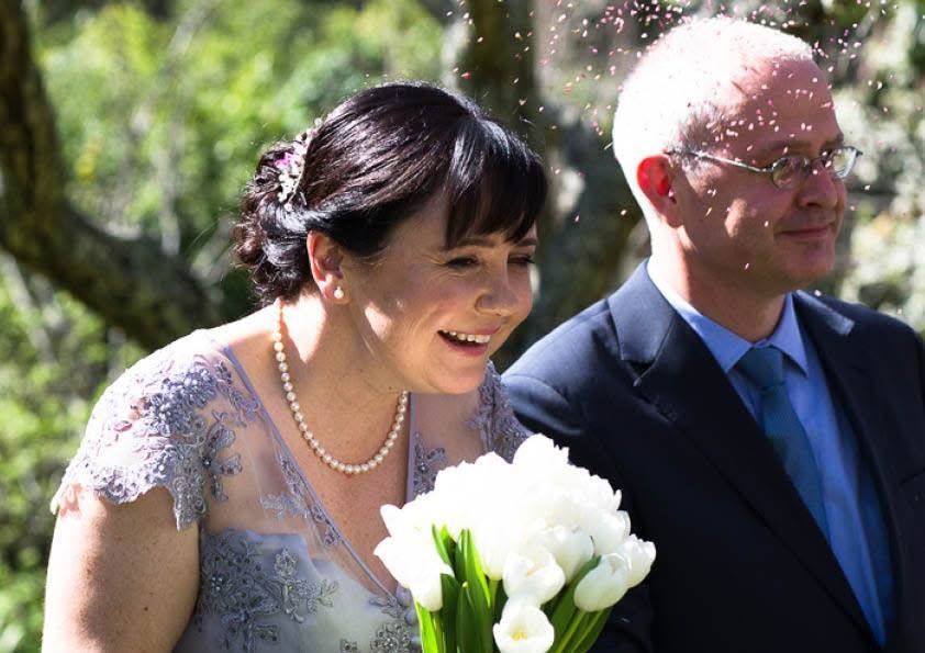 Joyful bride holding white tulip bouquet with groom as confetti falls during ceremony.