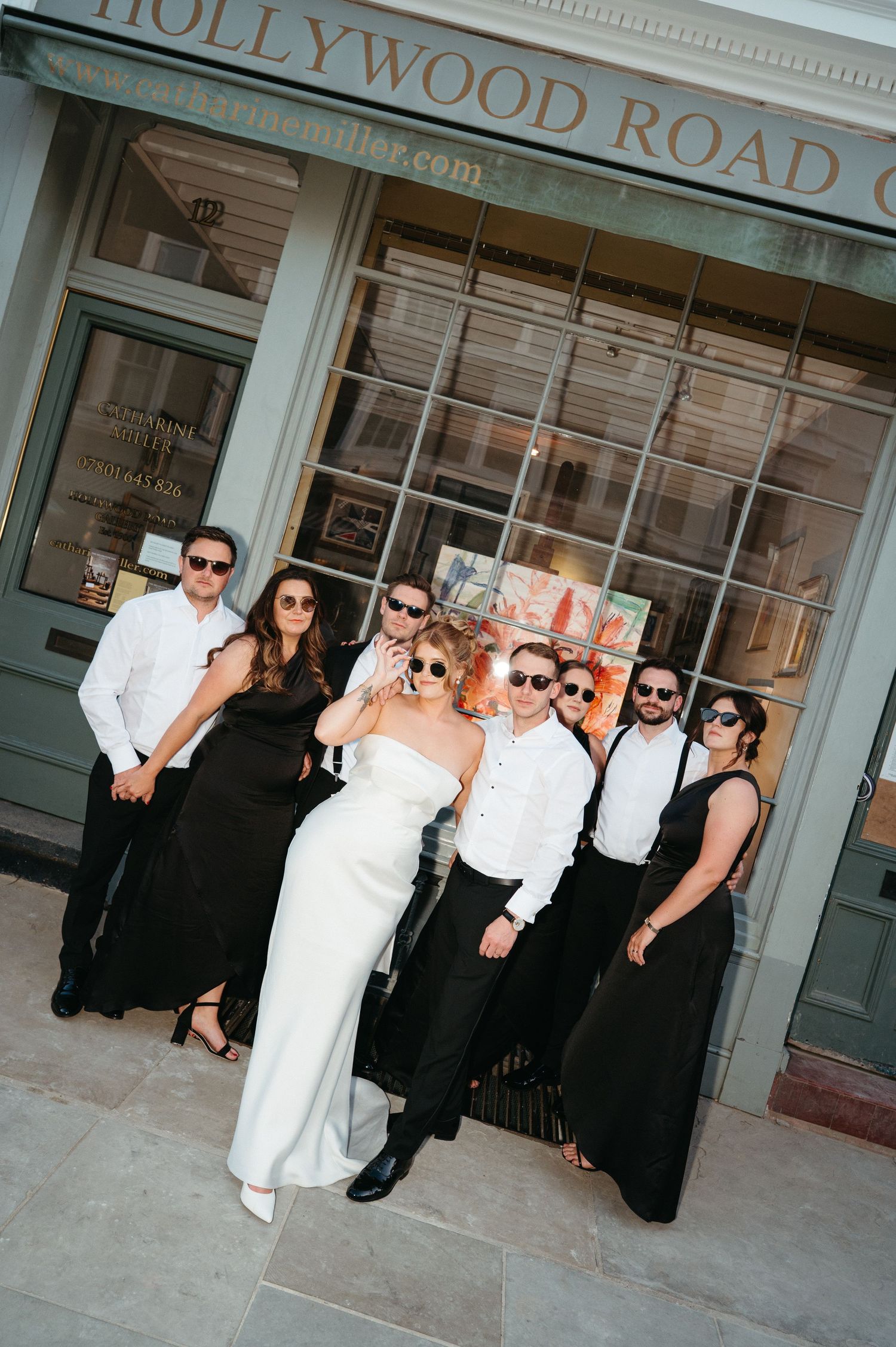 Wedding party walks and poses together on a grassy lawn in front of a white columned building on a sunny day.
