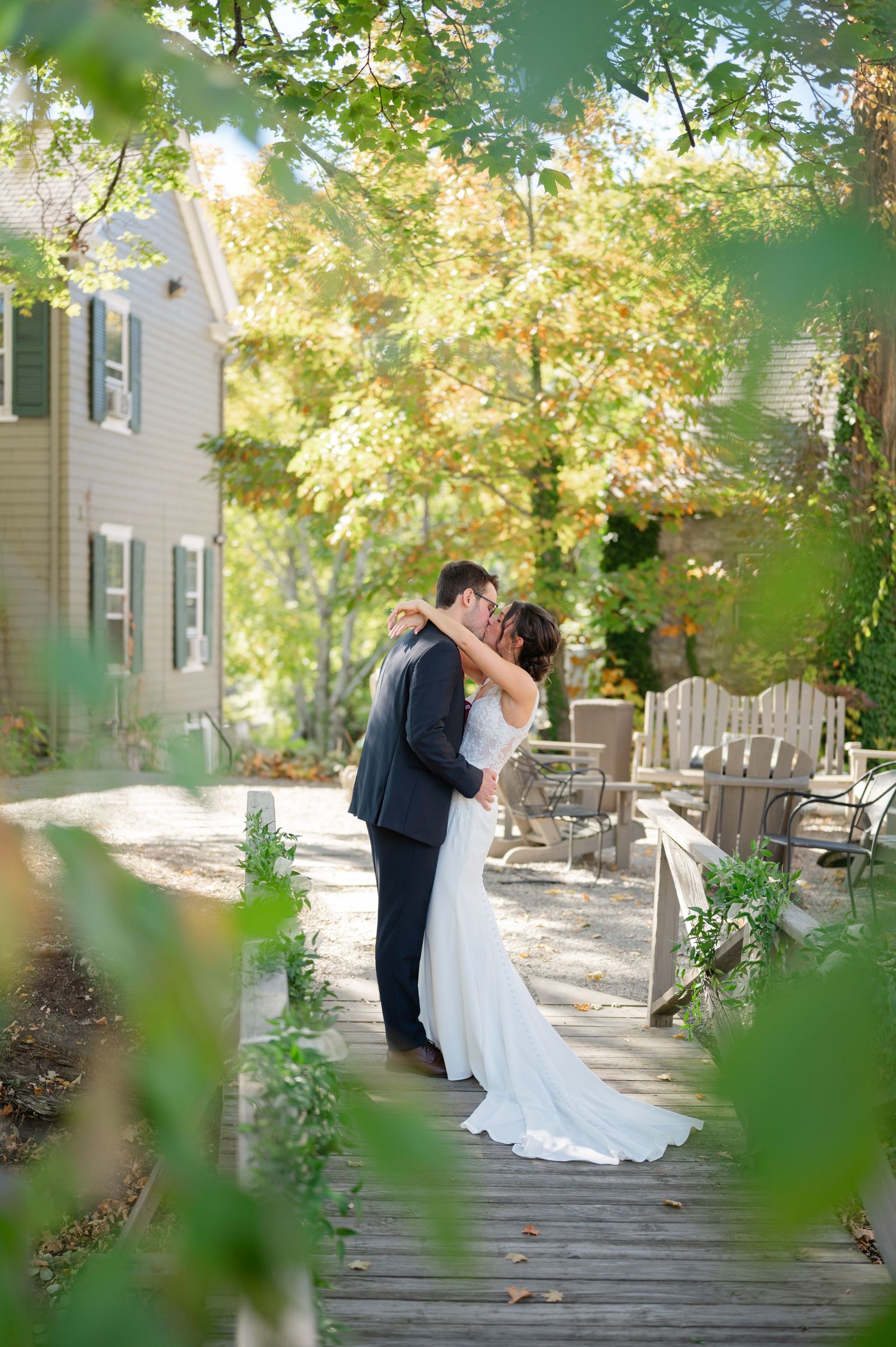 A romantic wedding portrait of a couple embracing in formal attire under a wooden pavilion.