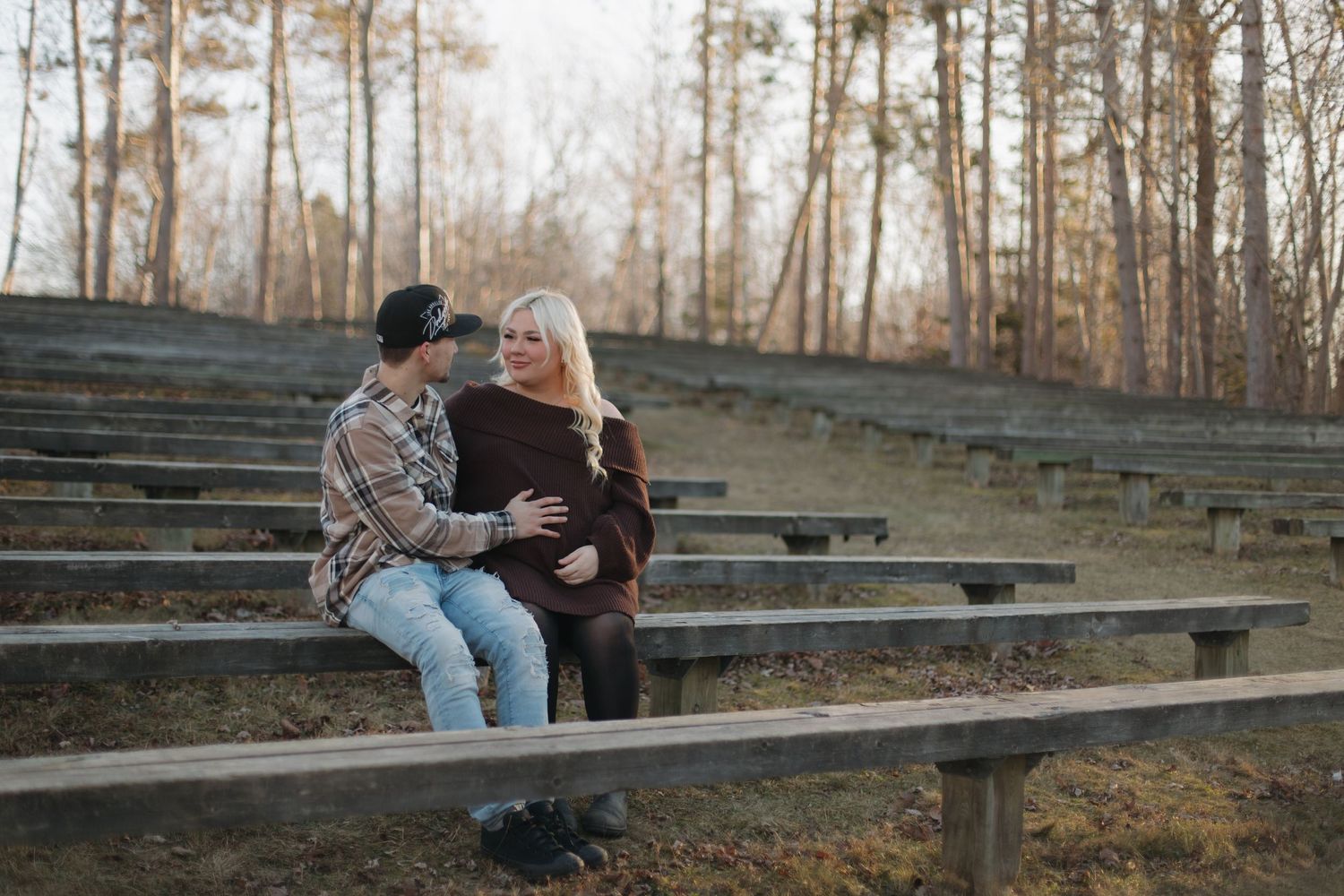 Two people sit together on concrete stadium bleachers during golden hour in a wooded setting.
