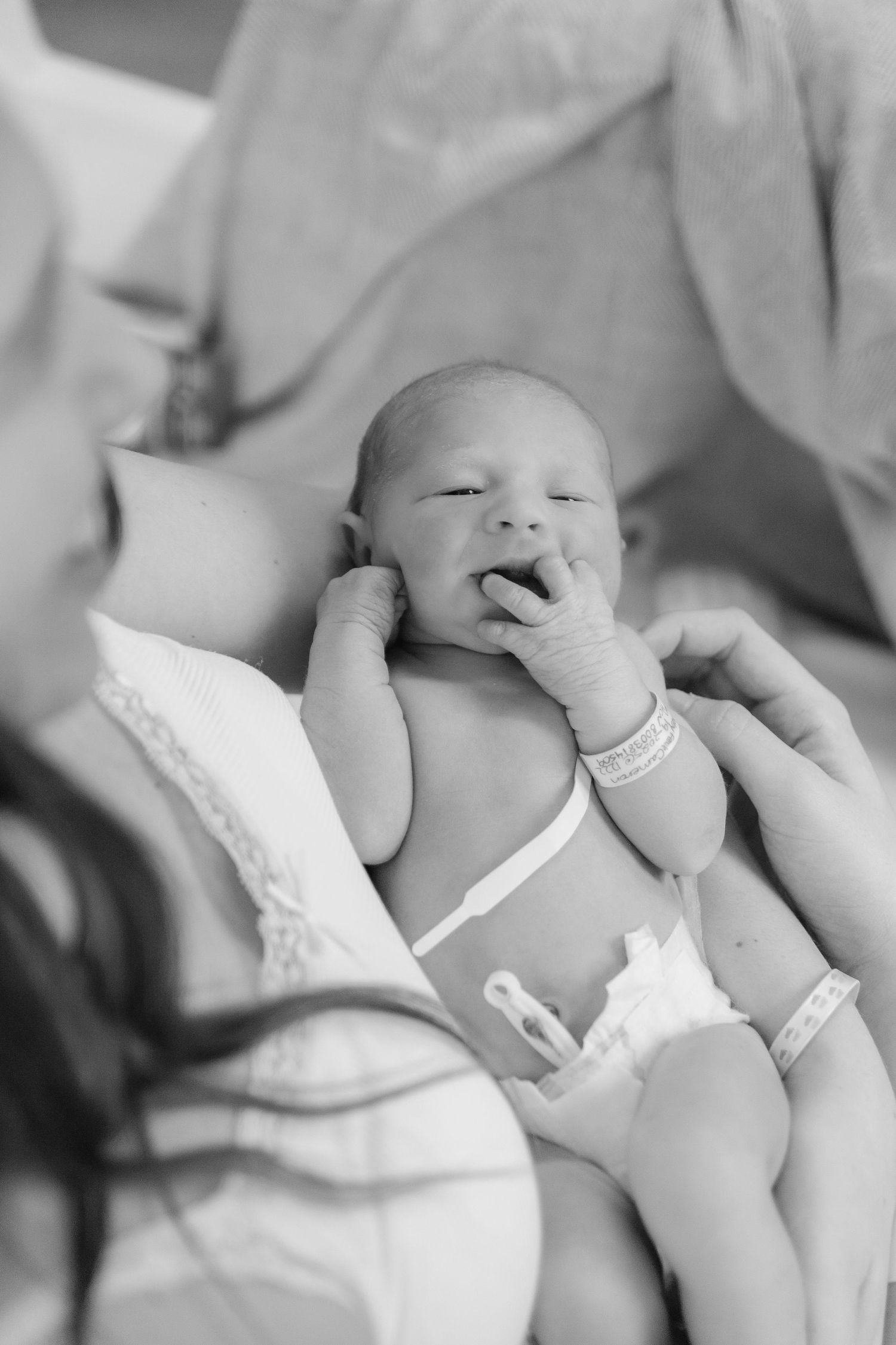 Black and white photo of a newborn baby yawning while lying on soft white fabric.