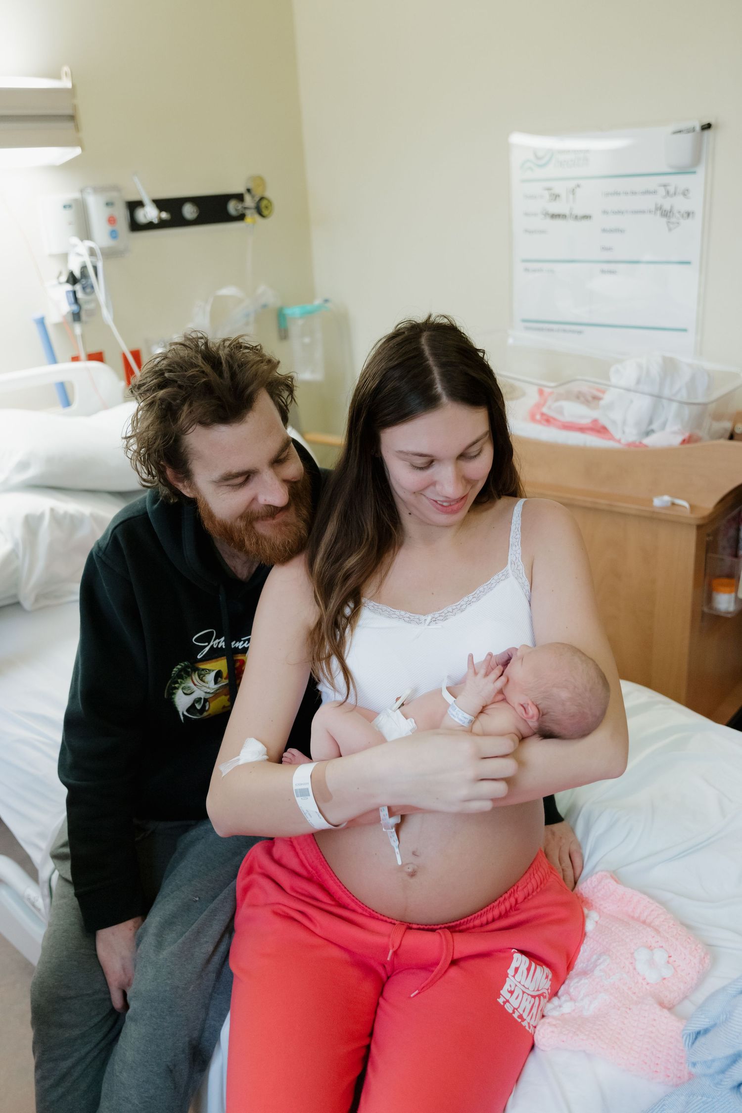 New parents share a tender moment with their newborn baby in a hospital room after birth.