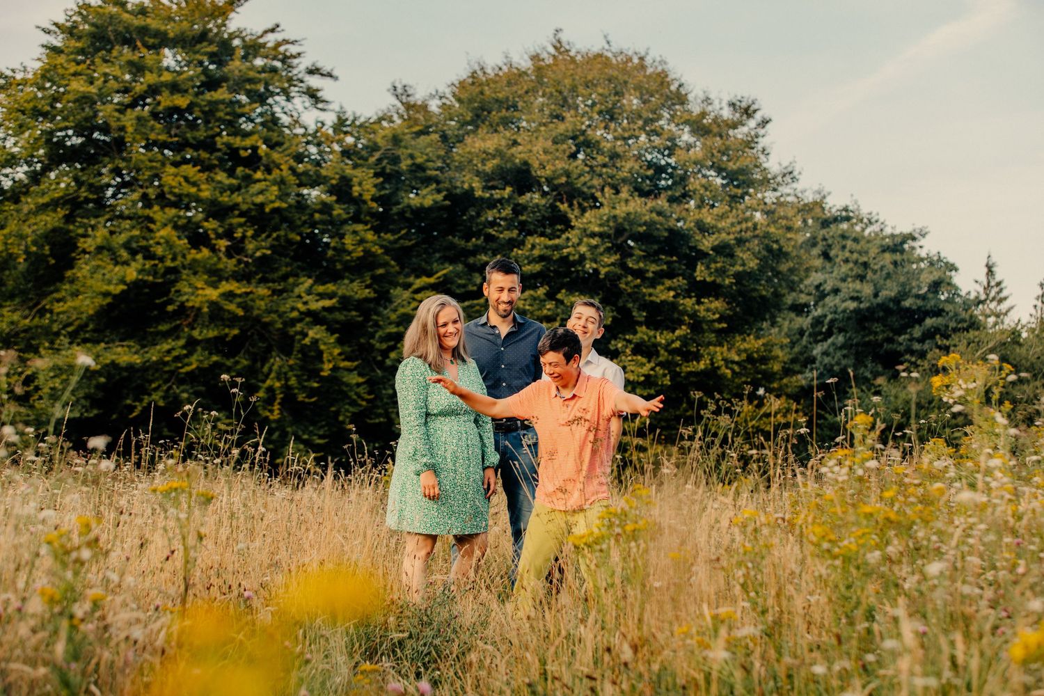 A family of four laugh and play together in a meadow