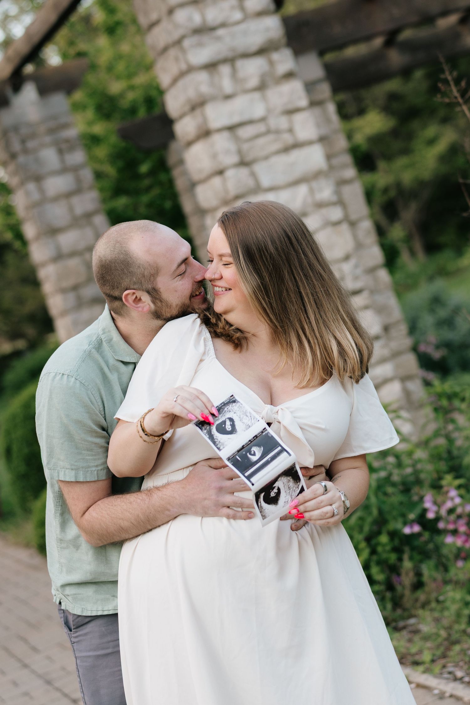 A romantic black and white wedding portrait shows a couple in formal attire embracing outside a white building.