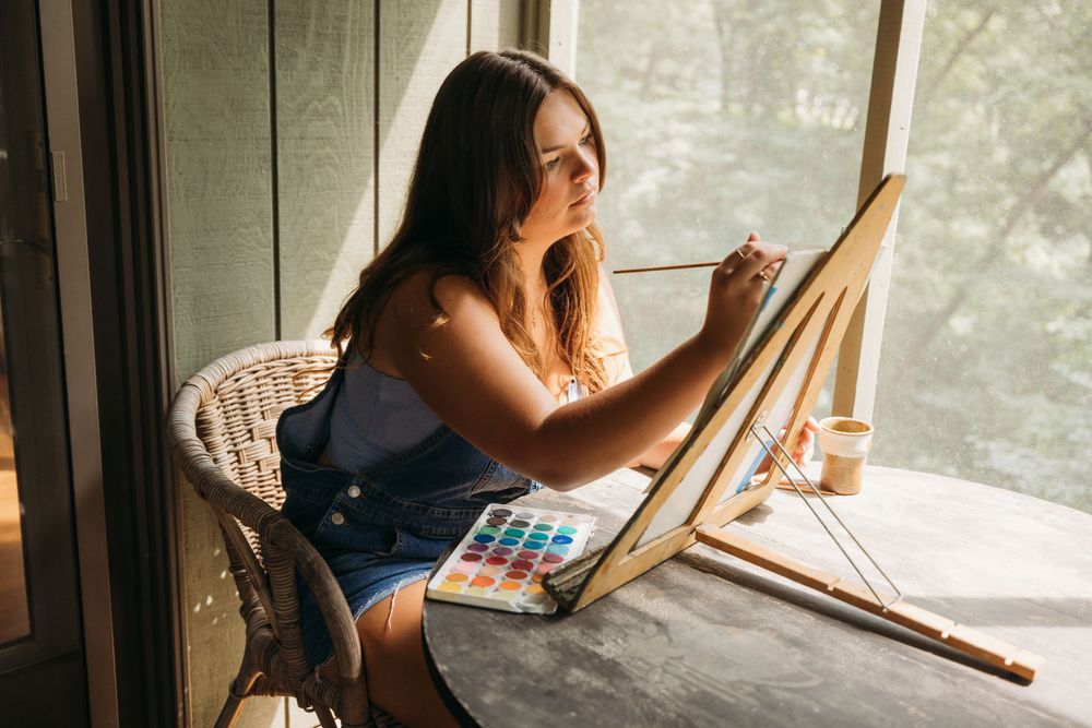 A young girl painting on a small easel with watercolors at an outdoor table, enjoying a creative art session.