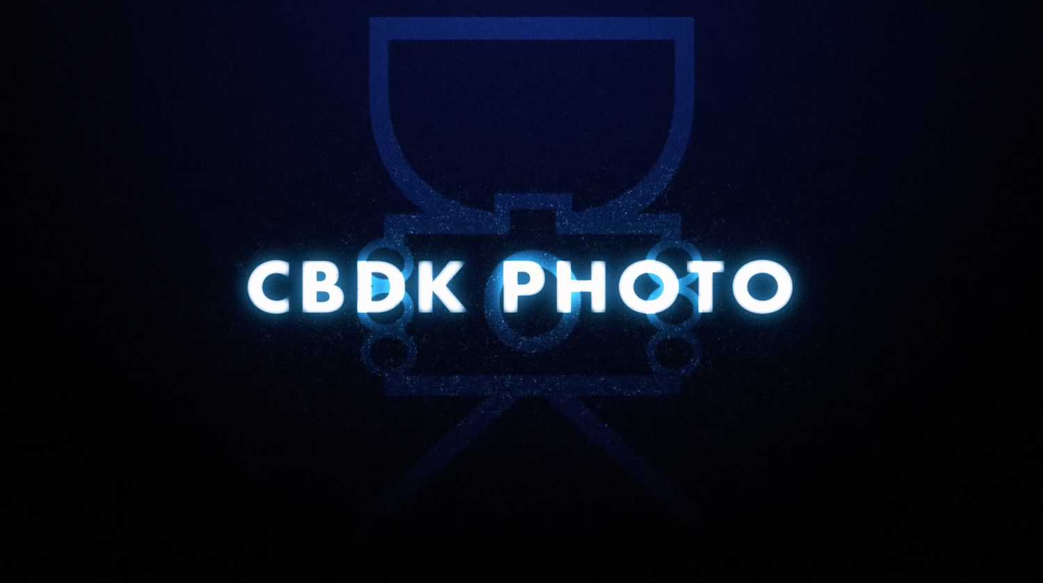 A glowing blue neon logo design for CBDK PHOTO featuring a minimal camera lens icon against a dark background.