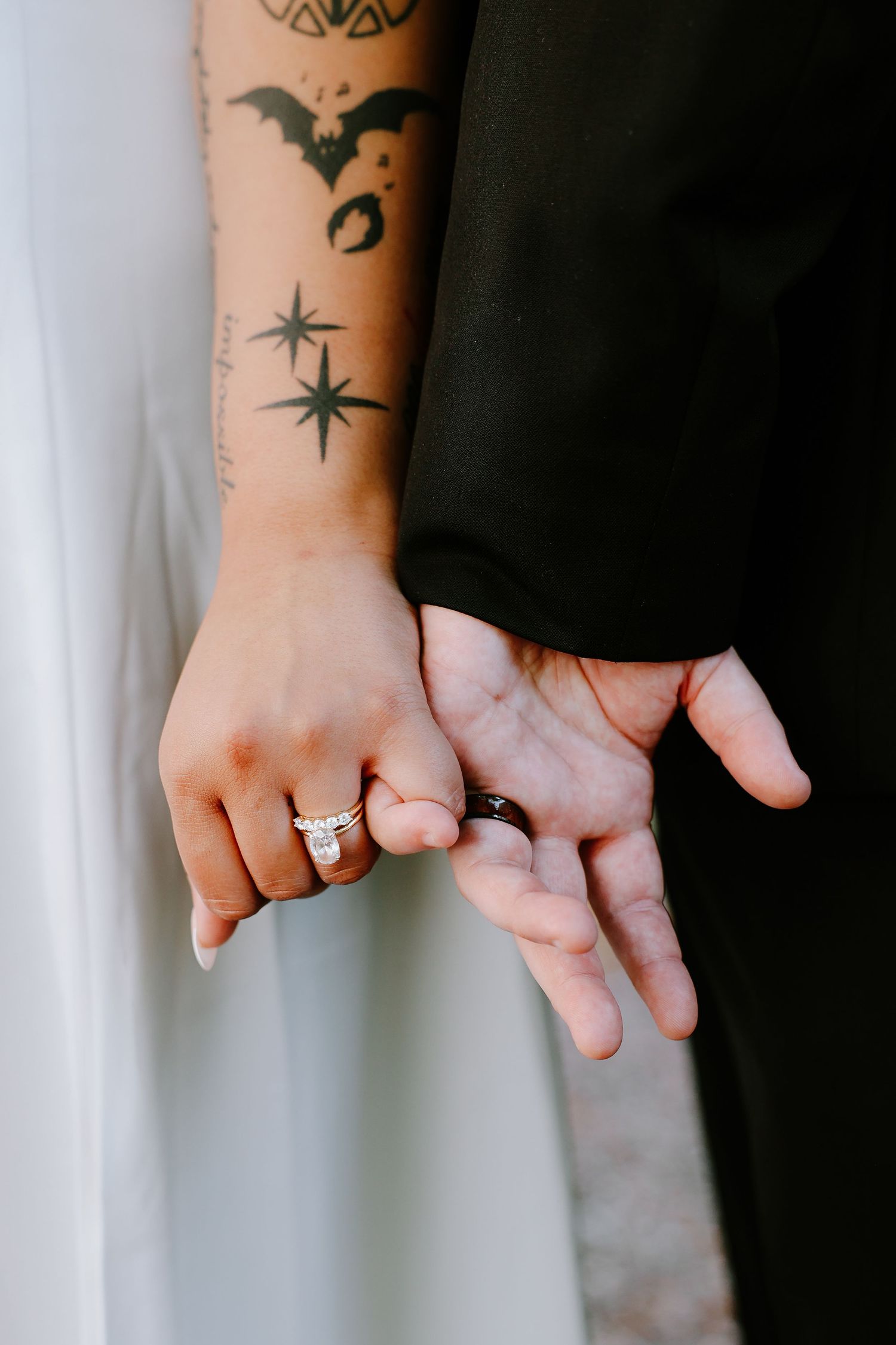 Close-up of bride and groom holding hands showing wedding rings and tattoos.