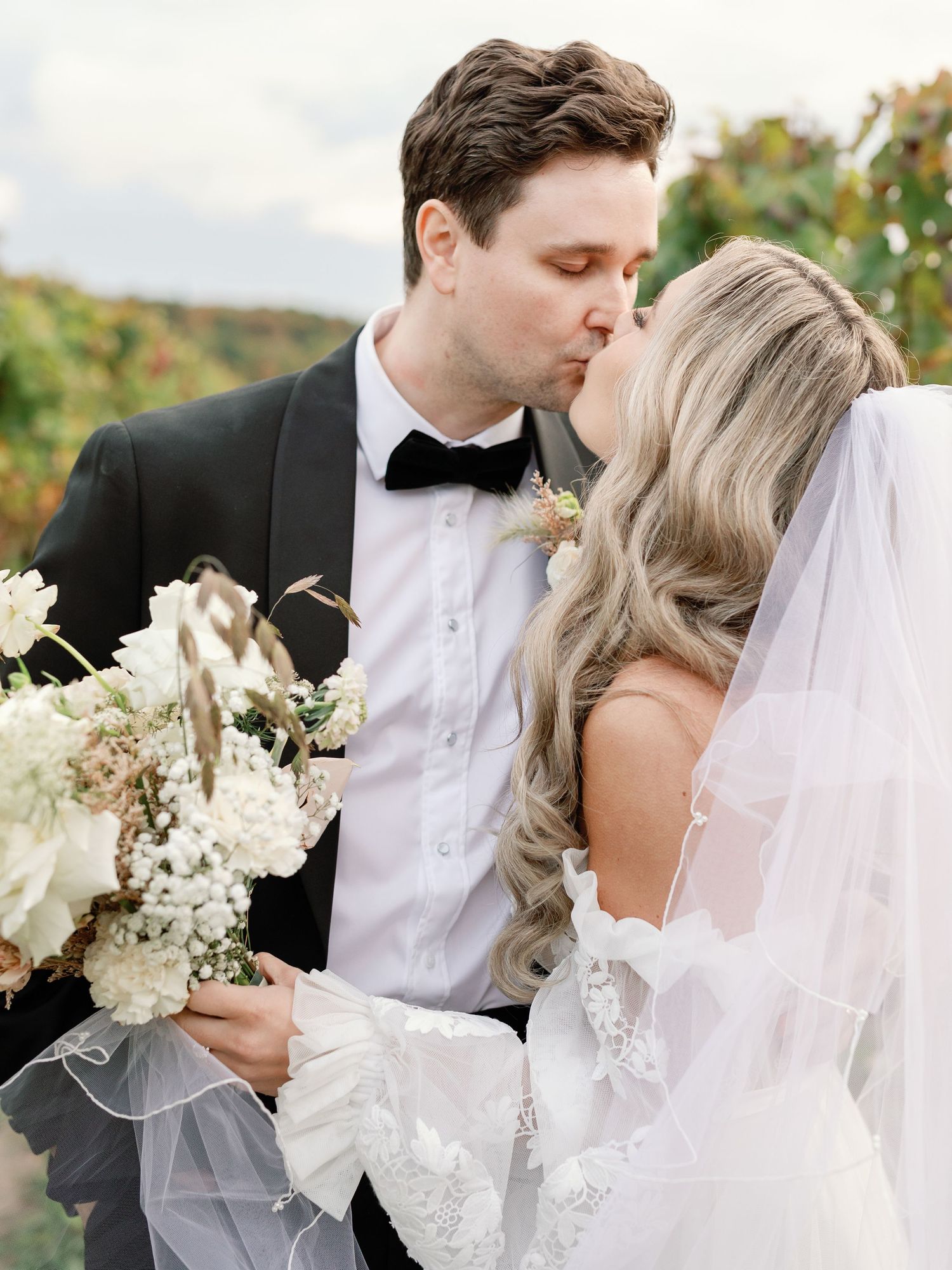 A bride and groom share a sweet kiss at Cave Springs, the bride holds a flower bouquet in one hand. Photo: Katie Crane