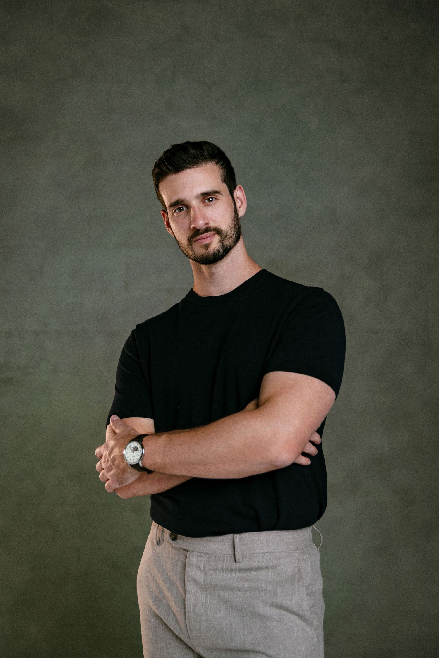 Professional headshot photography of a man with beard wearing a black shirt, arms crossed, photographed on a textured studio backdrop.