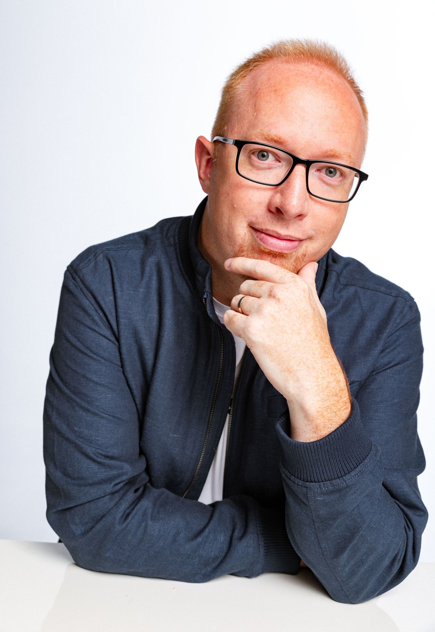 Professional headshot photography of a man wearing glasses, posed with hand on chin against a clean white studio background.