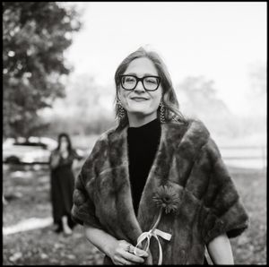 Black and white portrait of someone in glasses and a fur stole smiling outdoors on a misty day. Taken on film