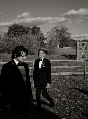 Black and white scenic shots capture father and son in formalwear walking through an autumn field at dusk right before a wedding