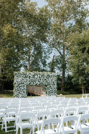 Outdoor wedding ceremony setup with white chairs and floral arch backdrop.