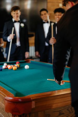 Groomsmen in formal attire gathered around pool table during wedding celebration.